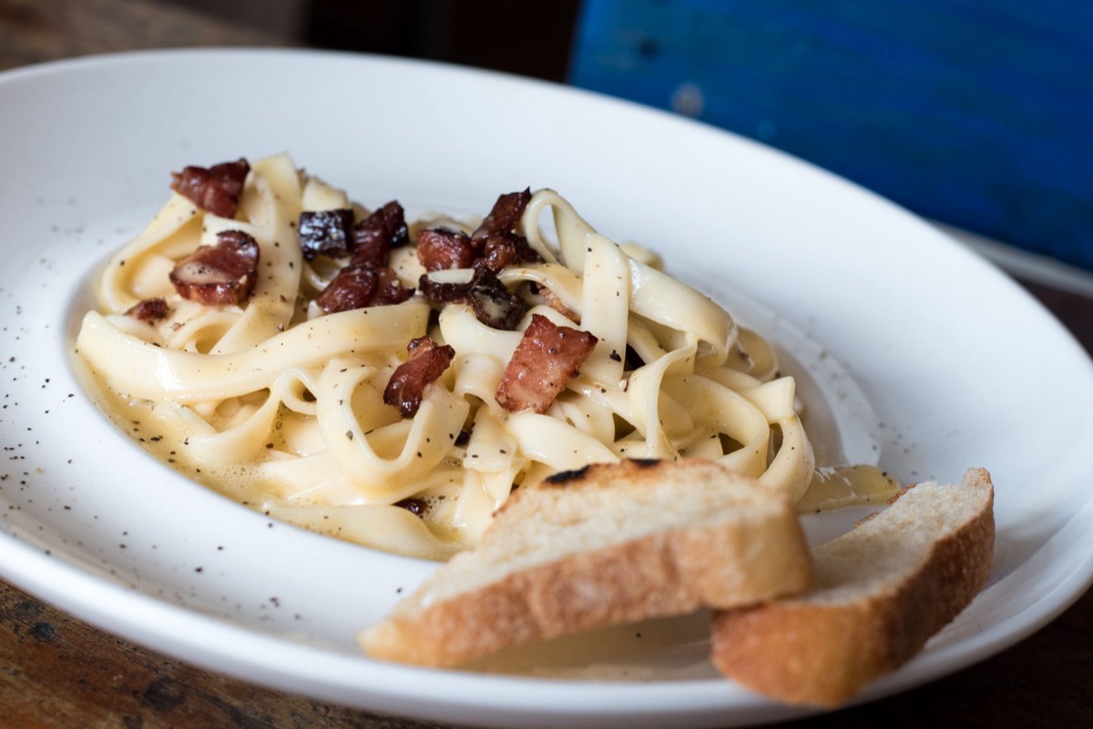 Creamy carbonara pasta with grated parmesan cheese in a white ceramic bowl.