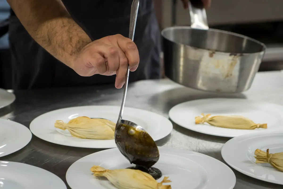 Chef plating gourmet dishes with sauce in a professional kitchen setting, showcasing culinary skills.