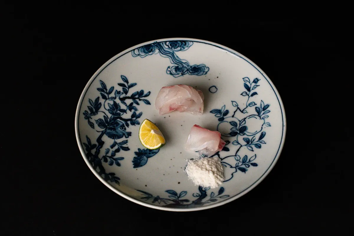 Artistic presentation of Japanese sashimi on a decorative plate with lemon and wasabi.