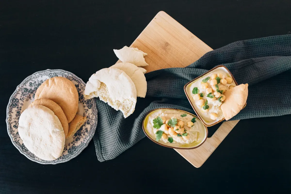 Top view of delicious creamy hummus with pita bread on a wooden board.