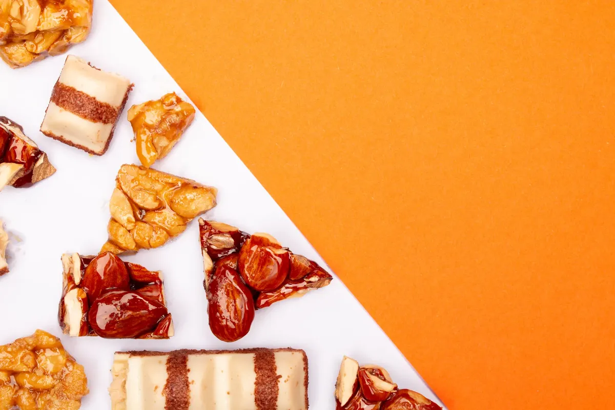 Delicious assortment of caramel and nut bars on bright orange and white surface, perfect for food photography.