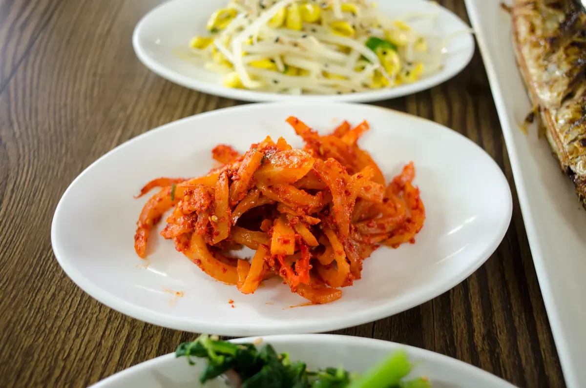 A vibrant collection of Korean side dishes featuring spicy kimchi, fresh greens, and bean sprouts.